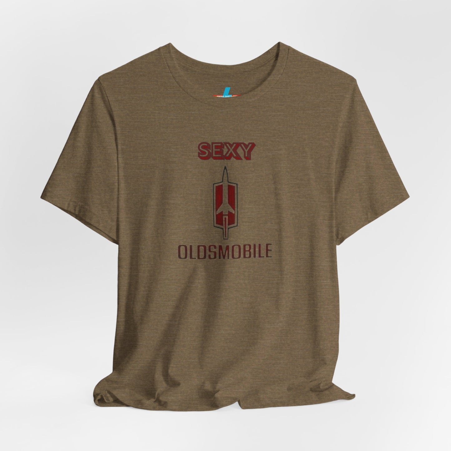 Introducing the Sexy Oldsmobile - Unisex Jersey Short Sleeve Tee by Printify, a light gray t-shirt featuring a striking graphic in the center. The design includes the word "SEXY" in bold red letters above a vertical Oldsmobile logo, underlined by the word "OLDSMOBILE" in red letters. This t-shirt is perfect for vintage car enthusiasts and comedy lovers alike, with its plain white background accentuating the bold design.