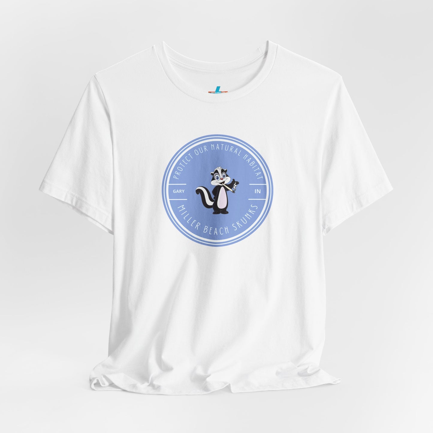 The Printify Miller Beach Skunks - Unisex Jersey Short Sleeve Tee is a gray T-shirt that features a circular blue logo at the center. Inside the logo, there is an illustration of a skunk with the text "Protect Our Habitat" and "Miller Beach Skunks" around the border, promoting environmental consciousness. The upper left part of the logo reads "Gary, IN.