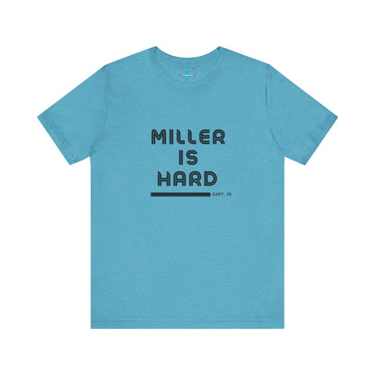 A unisex jersey short sleeve tee from Printify in burnt orange features the bold black text "MILLER IS HARD" on the chest, with "GARY, IN" written beneath in smaller black font. Perfect for showcasing Miller Beach's iconic spirit, this t-shirt is displayed against a plain white background.