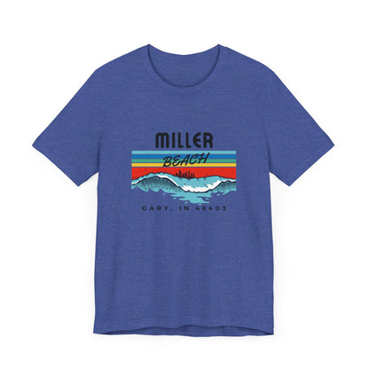 The Miller Beach 46403 Surf Style - Unisex Jersey Short Sleeve Tee by Printify features a retro surf-inspired design on a yellow background. The shirt displays "MILLER BEACH" above waves with a skyline illustration, while "Cary, IN 46403" is printed below the waves. The vibrant design also includes colorful stripes in shades of blue, red, and orange.