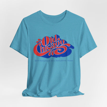 The "Old Chicago Mall Bolingbrook 1980s Retro - Unisex Jersey Short Sleeve Tee" from Printify is a gray T-shirt showcasing a vintage design with the text "Old Chicago" in blue and red. Beneath the main text, the address "355 S. Bolingbrook Drive, Bolingbrook, Illinois" appears in smaller font, evoking 80s nostalgia of the Old Chicago Mall. The shirt is displayed against a white background.