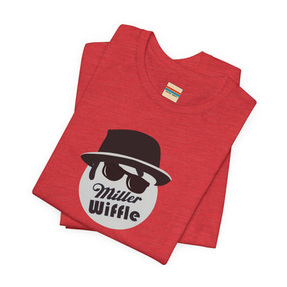 A purple unisex jersey tee from Printify, named the "Miller Wiffel Ball - Blues Brothers - Unisex Jersey Short Sleeve Tee," features a stylized graphic of a ball wearing a black fedora and sunglasses with the text "Miller Wiffel" below it. Another identical soft cotton t-shirt is neatly folded underneath, highlighting its breathable fabric.