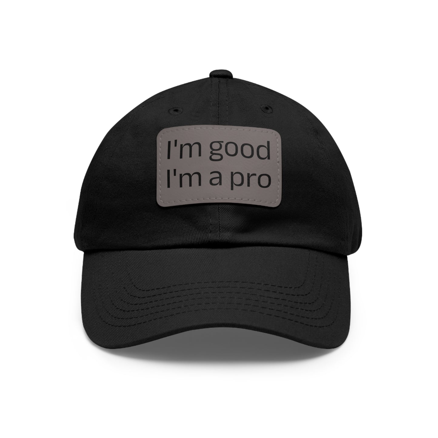 The Printify Dad Hat with Leather Patch (Rectangle) is a black, six-panel low-profile baseball cap made from bio-washed chino twill. This personalized Dad hat features a curved brim, visible stitching details, and a rectangular leather patch on the front that reads "I'm good I'm a pro" in grey text.