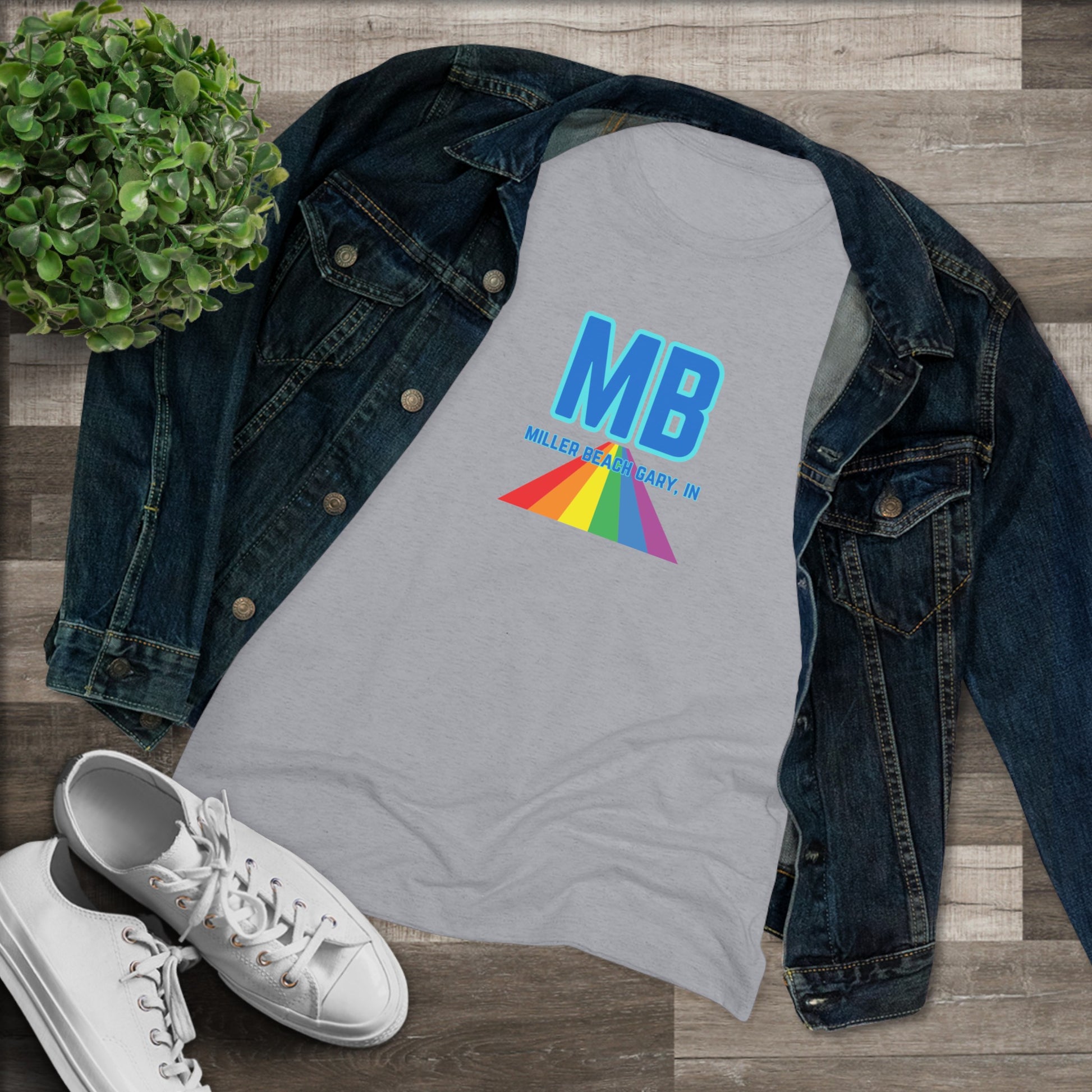 The Miller Beach Pride - Women's Triblend Tee by Printify is a dark gray, cozy t-shirt with a vintage look, featuring the text "MB" in large blue letters at the center. Below the letters, there is a rainbow-colored triangular design with "Millions & Binary, Inc." written in smaller text under the rainbow triangle.