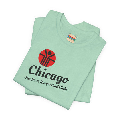 Two gray T-shirts are neatly folded on top of each other, with the top shirt showcasing the text "Chicago Health & Racquetball Clubs" in black below a red logo featuring a person with raised arms inside a circular design. This retro-inspired tee, named "Chicago Health Clubs 1980s Retro - Unisex Jersey Short Sleeve Tee" by Printify, is perfect for any fan of Chicago Health Clubs.