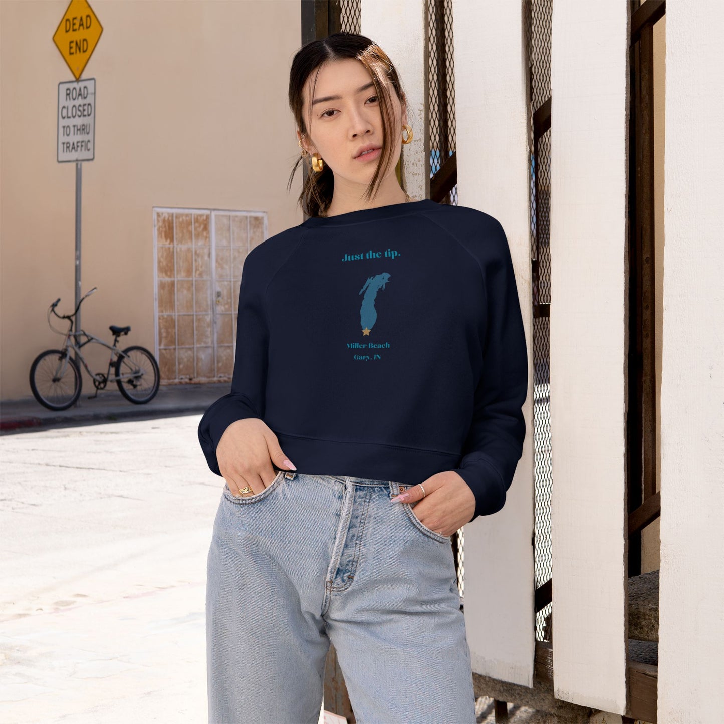 The "Just the Tip - Miller Beach" Women's Cropped Fleece Pullover by Printify is a beige sweatshirt with long sleeves and a crew neck. It features a blue-green abstract feather design in the center with the words "Just the tip" above it, and "Silly Peach" along with "Gary, IN." below. This pullover is crafted from premium tri-blend fabric for ultimate comfort and style.