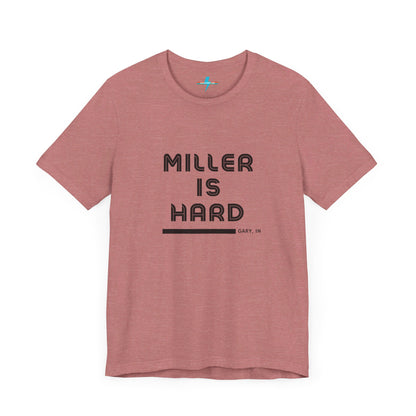 A unisex jersey short sleeve tee from Printify in burnt orange features the bold black text "MILLER IS HARD" on the chest, with "GARY, IN" written beneath in smaller black font. Perfect for showcasing Miller Beach's iconic spirit, this t-shirt is displayed against a plain white background.