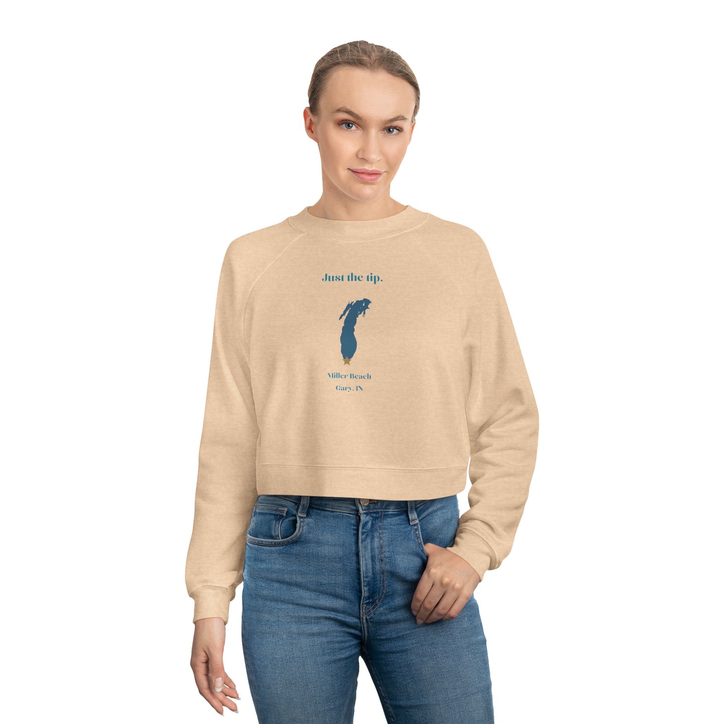 The "Just the Tip - Miller Beach" Women's Cropped Fleece Pullover by Printify is a beige sweatshirt with long sleeves and a crew neck. It features a blue-green abstract feather design in the center with the words "Just the tip" above it, and "Silly Peach" along with "Gary, IN." below. This pullover is crafted from premium tri-blend fabric for ultimate comfort and style.