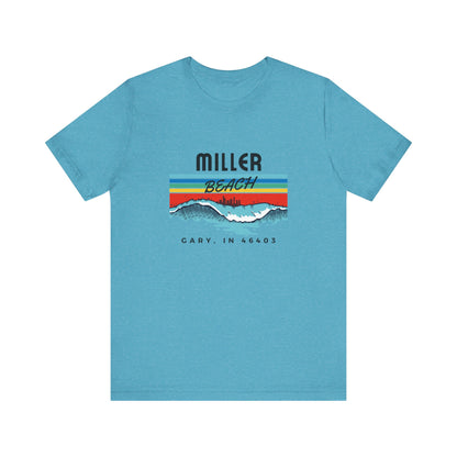 The Miller Beach 46403 Surf Style - Unisex Jersey Short Sleeve Tee by Printify features a retro surf-inspired design on a yellow background. The shirt displays "MILLER BEACH" above waves with a skyline illustration, while "Cary, IN 46403" is printed below the waves. The vibrant design also includes colorful stripes in shades of blue, red, and orange.