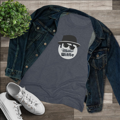 A cozy red t-shirt, the Miller Wiffel Ball - Blues Brothers - Women's Triblend Tee by Printify, features a graphic of a masked face wearing a fedora hat and sunglasses, along with the text "Miller Wiffle." The t-shirt is displayed on a wooden floor, paired with a denim jacket, white sneakers, and a potted green plant to create a vintage look.