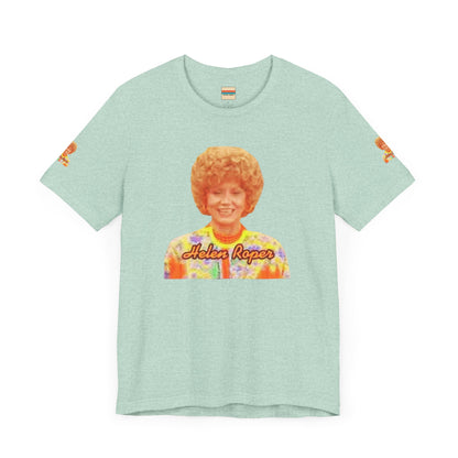 A lavender-colored Helen (Mrs.) Roper Three's Company - Unisex Jersey Short Sleeve Tee by Printify is hanging on a wooden hanger against a white background. This T-shirt features an image of a smiling person with curly hair wearing a colorful blouse, with the text "Helen Roper" underneath the image. Both sleeves have identical designs, making it perfect Three's Company merchandise.