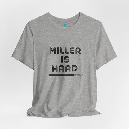 A unisex jersey short sleeve tee from Printify in burnt orange features the bold black text "MILLER IS HARD" on the chest, with "GARY, IN" written beneath in smaller black font. Perfect for showcasing Miller Beach's iconic spirit, this t-shirt is displayed against a plain white background.