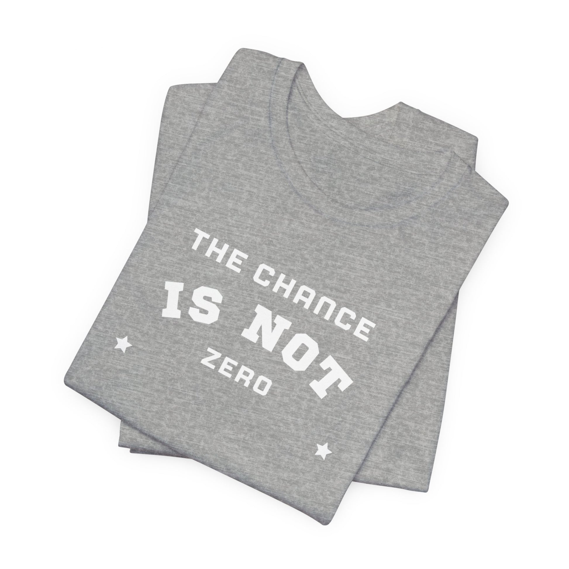 Folded light red Unisex Jersey Short Sleeve Tee from Printify, featuring bold white text that reads "THE CHANCE IS NOT ZERO" along with two star illustrations. This motivational T-shirt, made from breathable fabric, is neatly stacked with another identical shirt underneath.