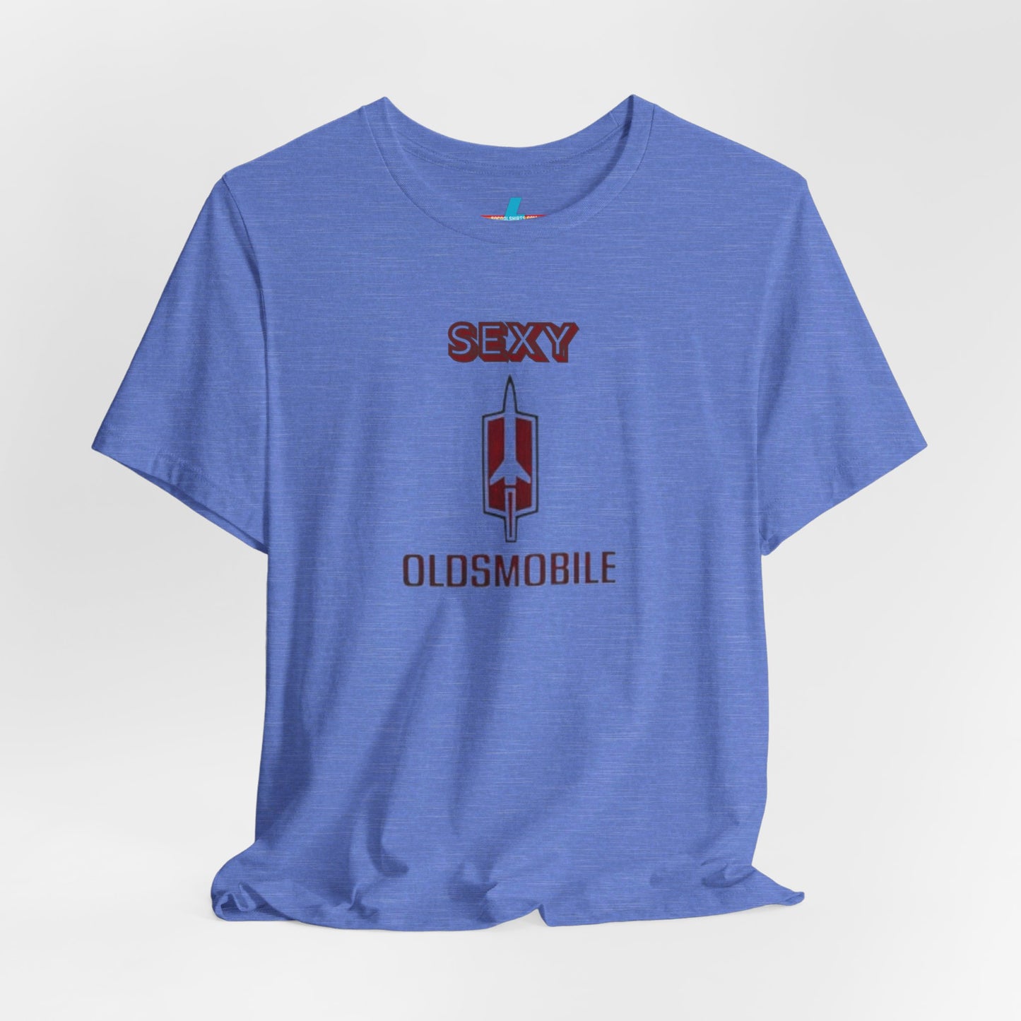 Introducing the Sexy Oldsmobile - Unisex Jersey Short Sleeve Tee by Printify, a light gray t-shirt featuring a striking graphic in the center. The design includes the word "SEXY" in bold red letters above a vertical Oldsmobile logo, underlined by the word "OLDSMOBILE" in red letters. This t-shirt is perfect for vintage car enthusiasts and comedy lovers alike, with its plain white background accentuating the bold design.