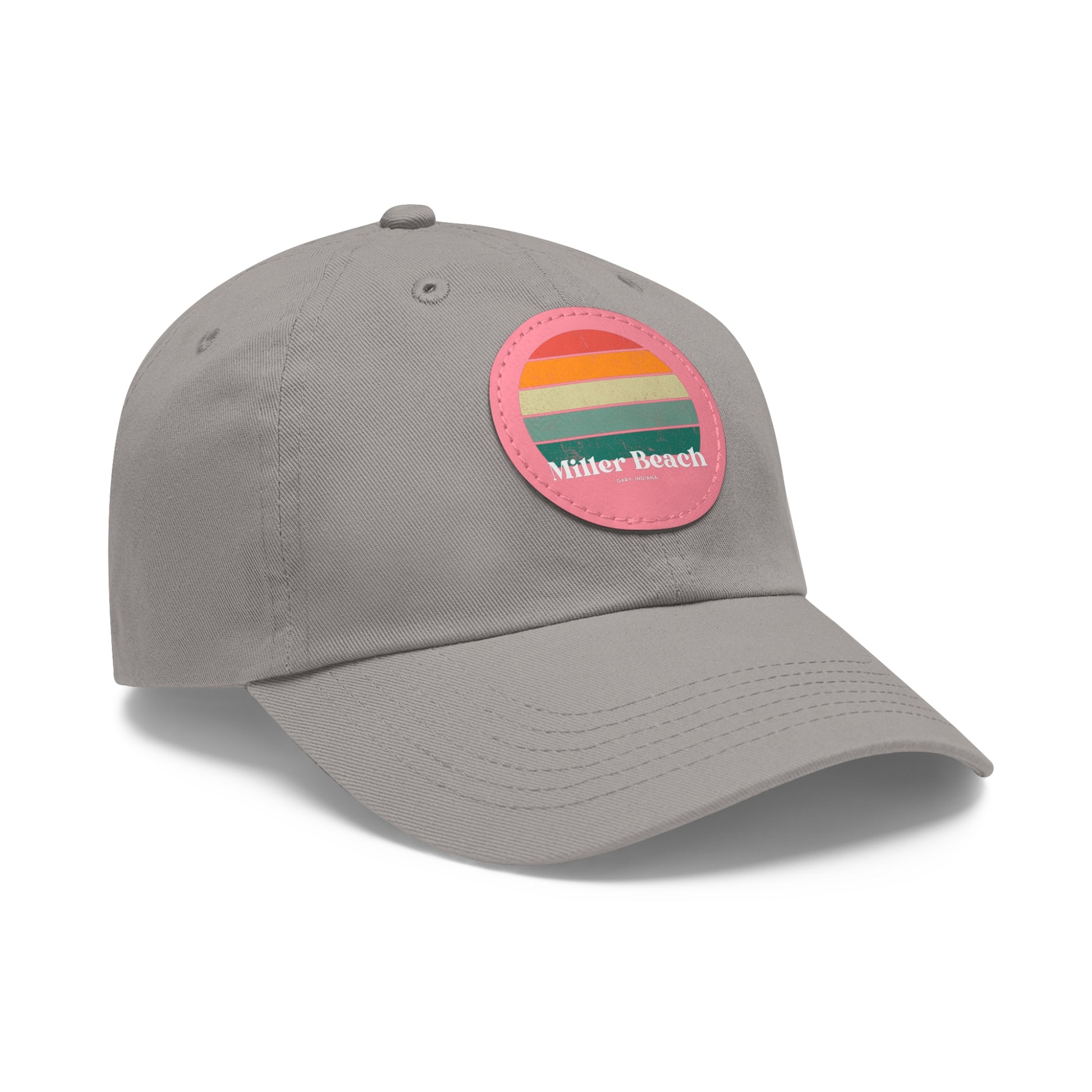 The Miller Beach Retro Sunset - Dad Hat with Leather Patch (Round) by Printify is a pink baseball cap crafted from bio-washed chino twill for added comfort. It features a PU leather patch adorned with horizontal stripes in red, orange, yellow, green, and blue. Below the stripes, "Miller Beach" is embroidered in white. An adjustable strap at the back ensures a perfect fit.