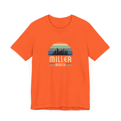 The Printify Miller Beach Chicago Skyline - Unisex Jersey Short Sleeve Tee is a light blue T-shirt featuring a stylized graphic of the Chicago skyline against a setting sun with gradient shades of blue and orange. Below the graphic, "Miller Beach" is printed in bold, yellow letters.