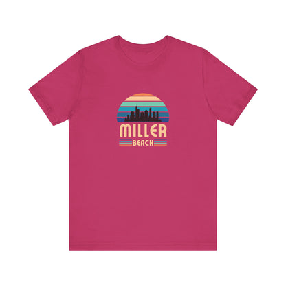 The Printify Miller Beach Chicago Skyline - Unisex Jersey Short Sleeve Tee is a light blue T-shirt featuring a stylized graphic of the Chicago skyline against a setting sun with gradient shades of blue and orange. Below the graphic, "Miller Beach" is printed in bold, yellow letters.