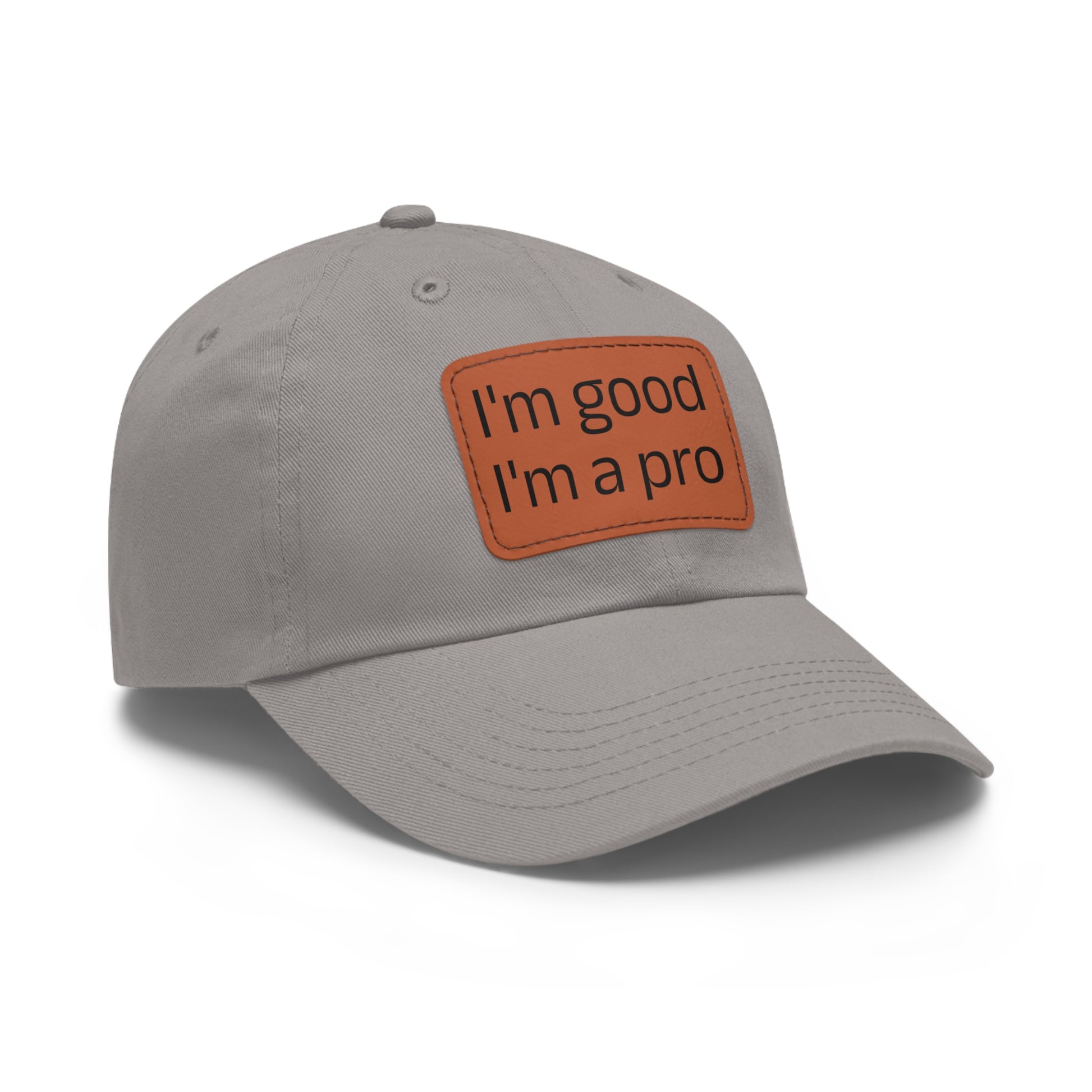 The Printify Dad Hat with Leather Patch (Rectangle) is a black, six-panel low-profile baseball cap made from bio-washed chino twill. This personalized Dad hat features a curved brim, visible stitching details, and a rectangular leather patch on the front that reads "I'm good I'm a pro" in grey text.