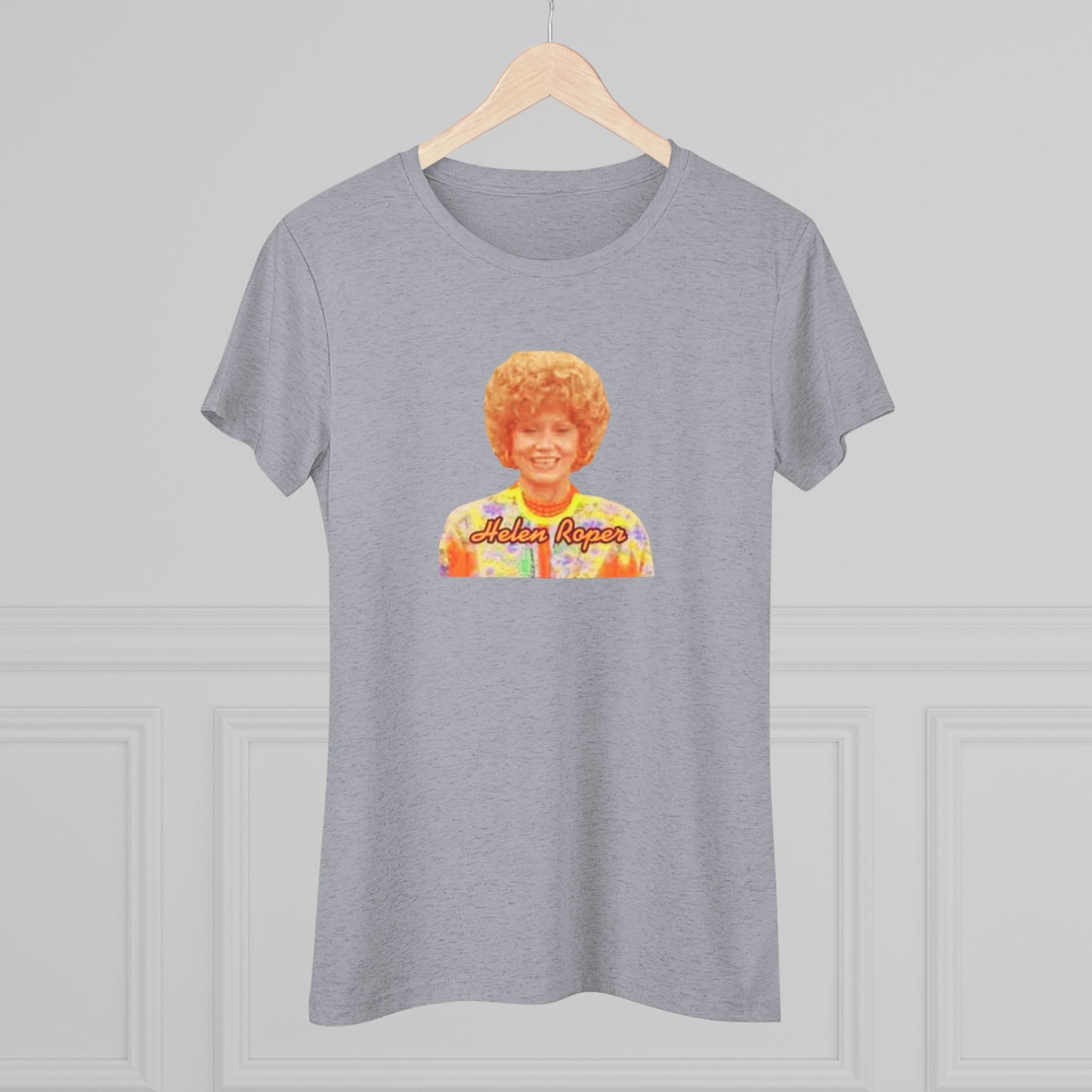 A Women's Triblend Tee by Printify, titled "Helen Roper - Three's Company," features a red design with an illustration of a smiling person with curly hair and colorful clothing. Below the illustration, the text "Helen Roper" is written in a bold, retro font, capturing the essence of vintage TV humor.