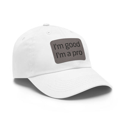 The Printify Dad Hat with Leather Patch (Rectangle) is a black, six-panel low-profile baseball cap made from bio-washed chino twill. This personalized Dad hat features a curved brim, visible stitching details, and a rectangular leather patch on the front that reads "I'm good I'm a pro" in grey text.