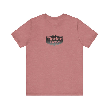 A light blue Printify "The Tinder Box 1980s" unisex jersey short sleeve tee featuring the "Tinder Box" logo in the center. The logo consists of a dark shield with the words "Tinder Box" in white text, with a small flame icon replacing the dot above the "i".