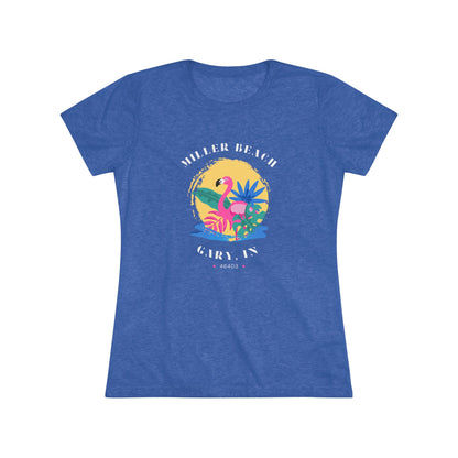 A women's triblend tee from Printify, the Miller Beach Flamingo features a blue color and "Miller Beach Gary, IN 46403" text with a vibrant design of a flamingo amidst tropical foliage for a vintage aesthetic. This t-shirt is showcased on a wooden surface alongside a denim jacket, white sneakers, and a potted plant.