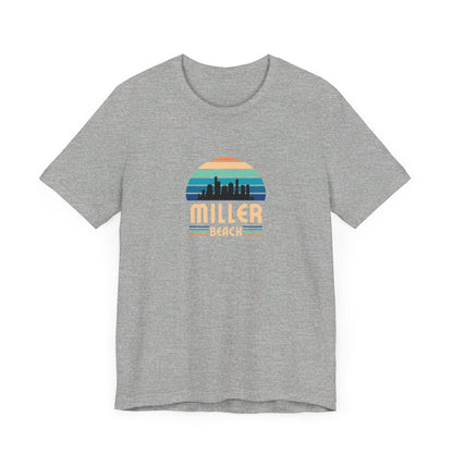 A brown unisex jersey short sleeve tee called "Miller Beach Chicago Skyline" from Printify features a vintage-style design with a sunset, the Chicago skyline, and "Miller Beach" in bold letters. The design incorporates shades of blue, orange, and yellow and is displayed against a plain white background.