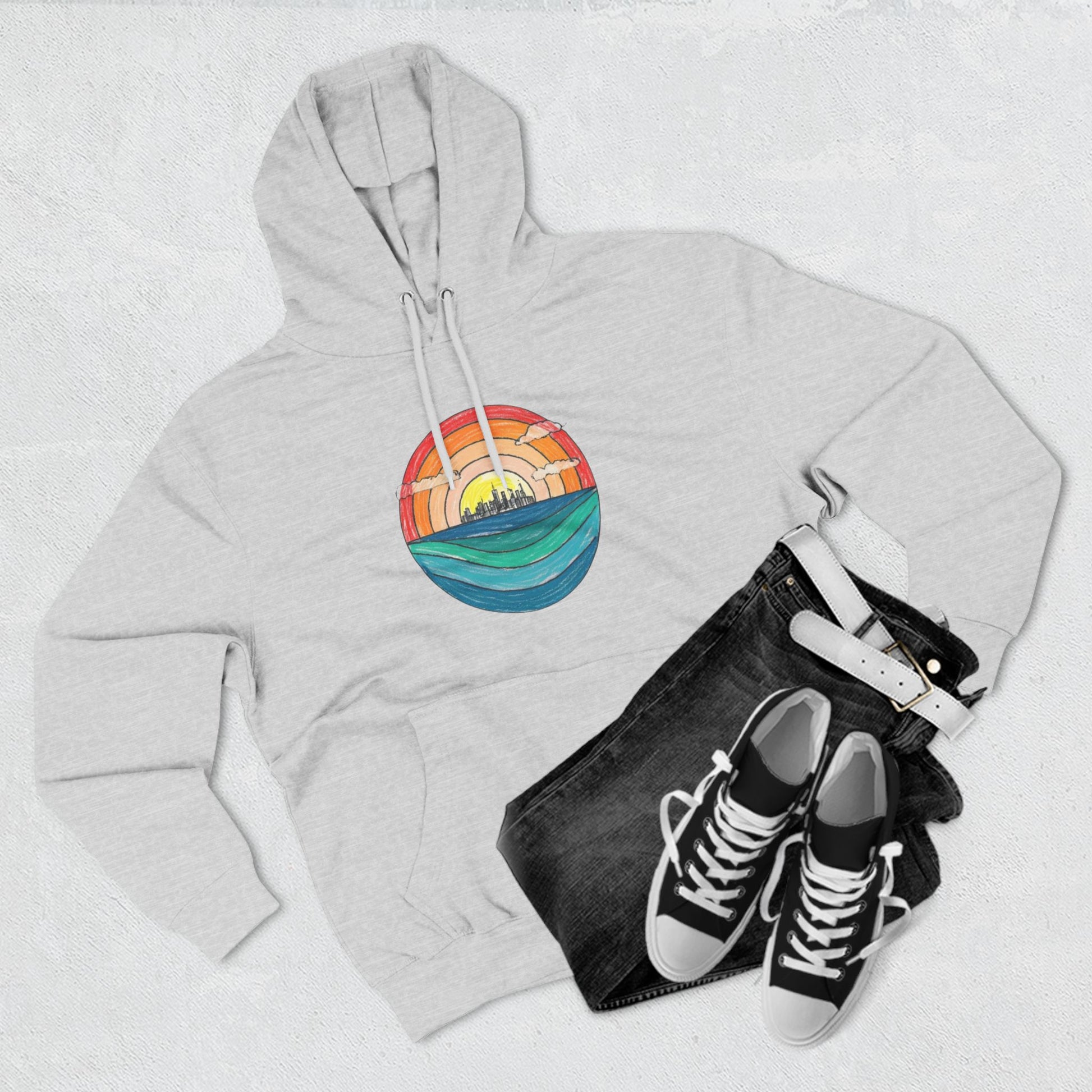 The Miller Beach Abstract - Three-Panel Fleece Hoodie by Printify is a premium light gray pullover featuring a vibrant circular front design. It showcases an abstract sunset-over-ocean scene with blue waters, an orange to red gradient sky, and a city skyline silhouette. Made from soft combed ring-spun cotton and lined with cozy fleece for extra warmth.