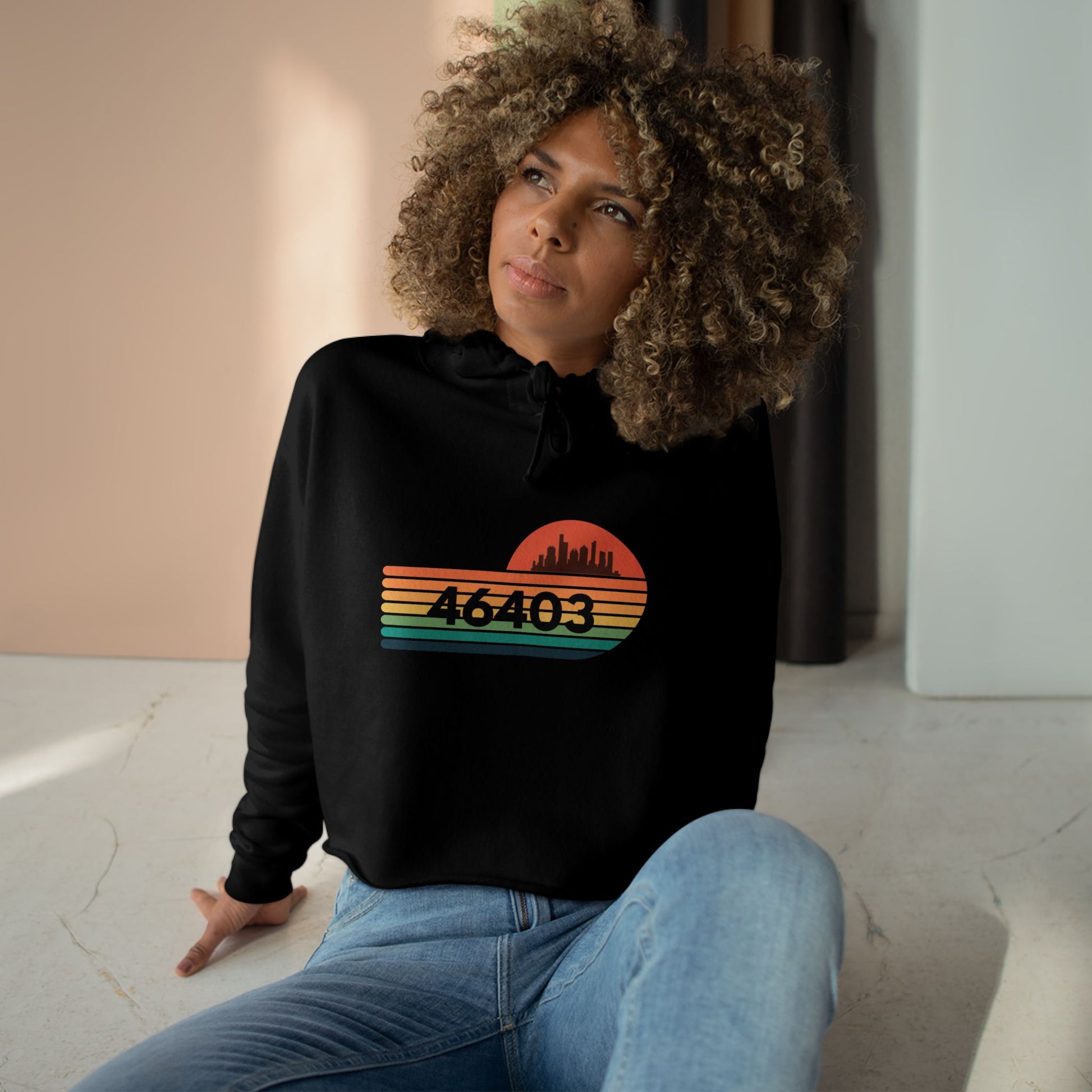 The Miller Beach 46403 Women's Crop Hoodie by Printify features a nostalgic design with a city skyline silhouette and the iconic "46403" zip code, set against a striped sunset backdrop in vibrant orange, green, and yellow hues that capture the essence of Miller Beach.