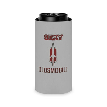 The Sexy Oldsmobile Koozie by Printify features "SEXY" in red at the top on a gray background, followed by the Oldsmobile logo and the word "OLDSMOBILE" below it. At the bottom, there's a blue and red logo reading "SOCOOLSHIRTS.COM." This koozie has an indentation designed to hold a can securely.