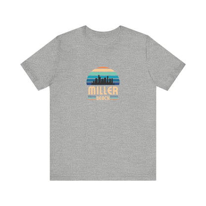 A brown unisex jersey short sleeve tee called "Miller Beach Chicago Skyline" from Printify features a vintage-style design with a sunset, the Chicago skyline, and "Miller Beach" in bold letters. The design incorporates shades of blue, orange, and yellow and is displayed against a plain white background.