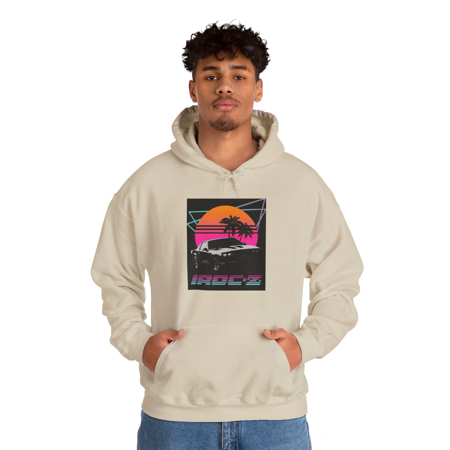 Introducing the Chevrolet IRoc Z28 - 1980s Retro Hoodie by Printify: This vibrant pink hoodie showcases a striking retro design on the front, featuring a classic American muscle car set against an orange and red sunset with palm trees, intersected by geometric shapes. The text "IROCZ" is prominently displayed below the image. Offering a relaxed fit and equipped with a front pocket, this hoodie perfectly captures the essence of 1980s style.