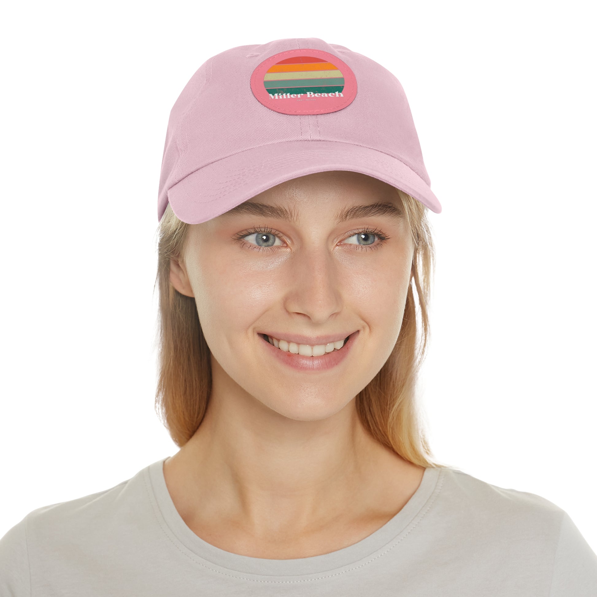 The Miller Beach Retro Sunset - Dad Hat with Leather Patch (Round) by Printify is a pink baseball cap crafted from bio-washed chino twill for added comfort. It features a PU leather patch adorned with horizontal stripes in red, orange, yellow, green, and blue. Below the stripes, "Miller Beach" is embroidered in white. An adjustable strap at the back ensures a perfect fit.