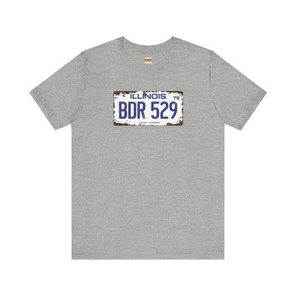 The Printify Blues Brothers BDR 529 License Plate Unisex Jersey Short Sleeve Tee showcases a vintage Illinois license plate graphic with "BDR 529" prominently displayed, as famously seen in the Blues Brothers film. The design includes "Illinois" and "Land of Lincoln" above and below the numbers, with a weathered, rustic look that enhances its retro appeal.