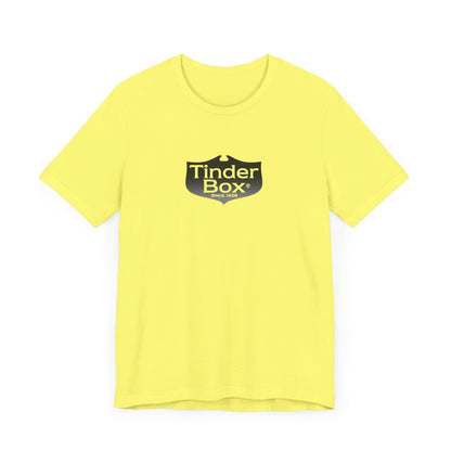 A light blue Printify "The Tinder Box 1980s" unisex jersey short sleeve tee featuring the "Tinder Box" logo in the center. The logo consists of a dark shield with the words "Tinder Box" in white text, with a small flame icon replacing the dot above the "i".