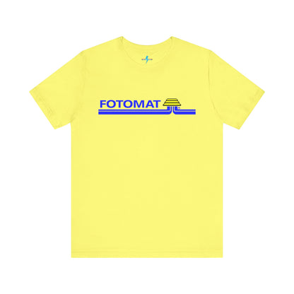 The Fotomat 1970s Retro T-Shirt by Printify is a dark gray short-sleeve shirt that features the word "FOTOMAT" in bold blue capital letters and a blue and yellow graphic design resembling layered lines and an upside-down triangle. This Tshirt captures the essence of 80s nostalgia with its centered, retro design.