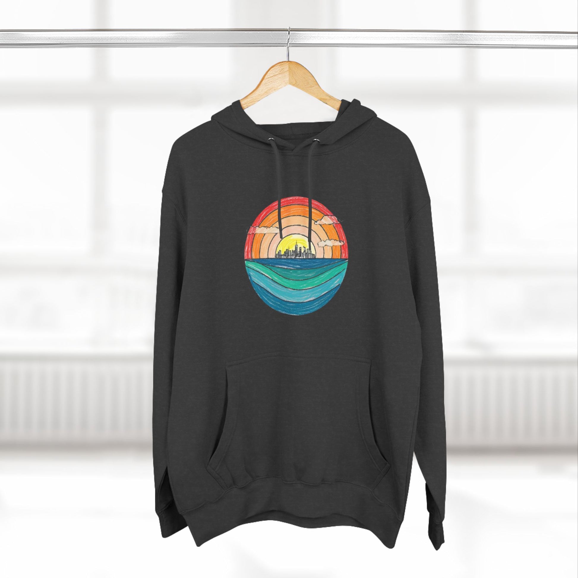 The Miller Beach Abstract - Three-Panel Fleece Hoodie by Printify is a premium light gray pullover featuring a vibrant circular front design. It showcases an abstract sunset-over-ocean scene with blue waters, an orange to red gradient sky, and a city skyline silhouette. Made from soft combed ring-spun cotton and lined with cozy fleece for extra warmth.