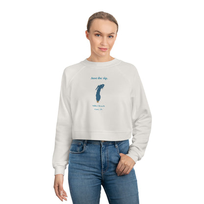 The "Just the Tip - Miller Beach" Women's Cropped Fleece Pullover by Printify is a beige sweatshirt with long sleeves and a crew neck. It features a blue-green abstract feather design in the center with the words "Just the tip" above it, and "Silly Peach" along with "Gary, IN." below. This pullover is crafted from premium tri-blend fabric for ultimate comfort and style.