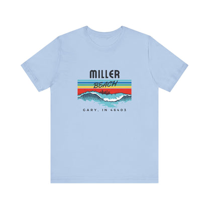 The Miller Beach 46403 Surf Style - Unisex Jersey Short Sleeve Tee by Printify features a retro surf-inspired design on a yellow background. The shirt displays "MILLER BEACH" above waves with a skyline illustration, while "Cary, IN 46403" is printed below the waves. The vibrant design also includes colorful stripes in shades of blue, red, and orange.