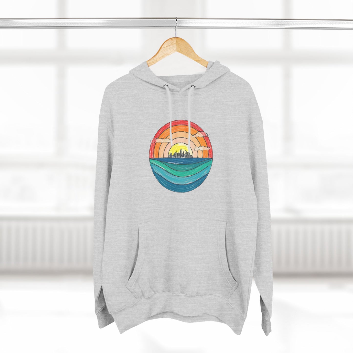 The Miller Beach Abstract - Three-Panel Fleece Hoodie by Printify is a premium light gray pullover featuring a vibrant circular front design. It showcases an abstract sunset-over-ocean scene with blue waters, an orange to red gradient sky, and a city skyline silhouette. Made from soft combed ring-spun cotton and lined with cozy fleece for extra warmth.