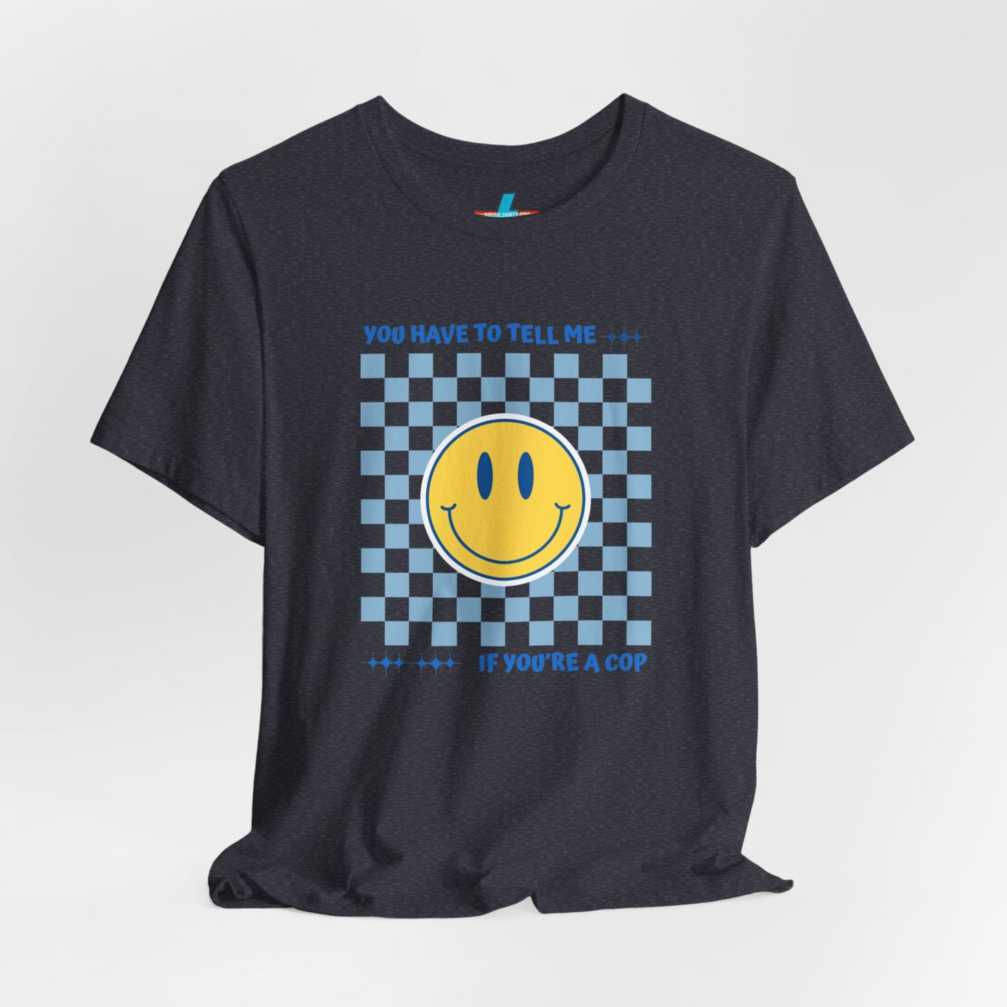 A light yellow unisex jersey short sleeve tee from Printify featuring a blue and yellow checkerboard pattern with a large yellow smiley face in the center. The shirt displays blue text above and below the pattern that reads, "You have to tell me if you're a cop." It's made from 100% Airlume combed and ring-spun cotton.