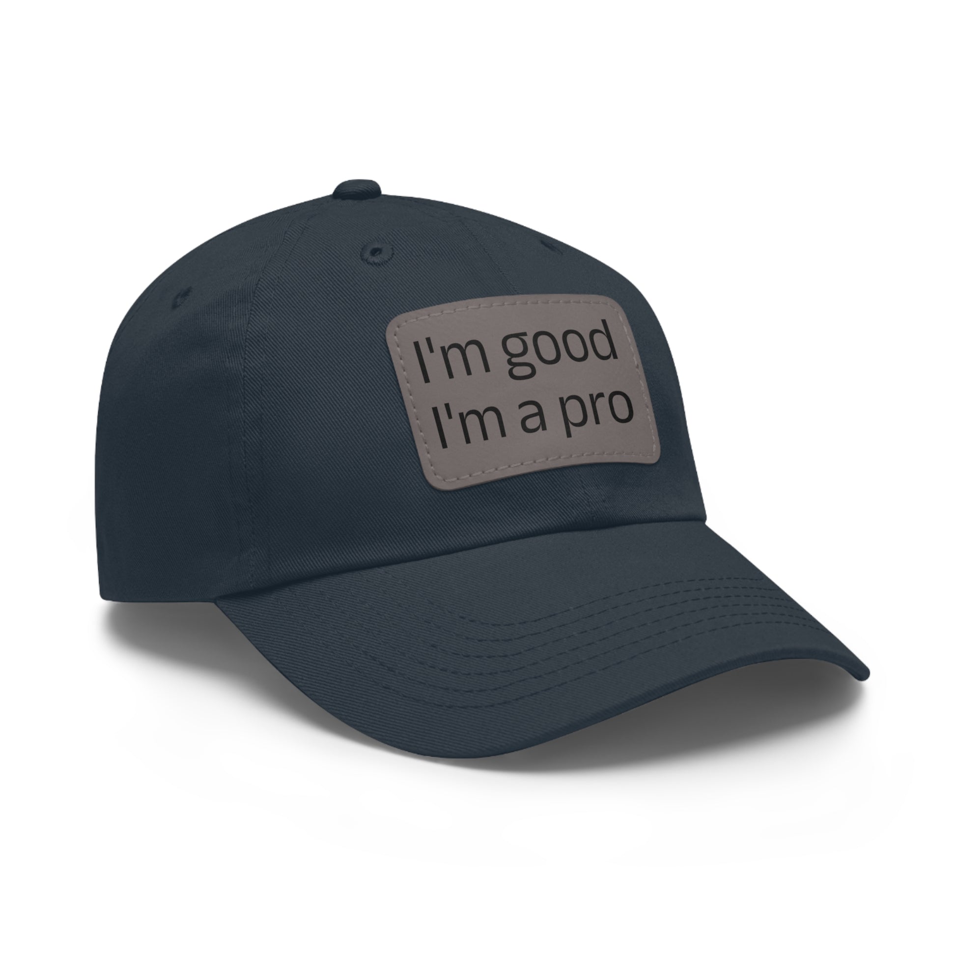 The Printify Dad Hat with Leather Patch (Rectangle) is a black, six-panel low-profile baseball cap made from bio-washed chino twill. This personalized Dad hat features a curved brim, visible stitching details, and a rectangular leather patch on the front that reads "I'm good I'm a pro" in grey text.