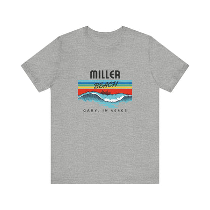 The Miller Beach 46403 Surf Style - Unisex Jersey Short Sleeve Tee by Printify features a retro surf-inspired design on a yellow background. The shirt displays "MILLER BEACH" above waves with a skyline illustration, while "Cary, IN 46403" is printed below the waves. The vibrant design also includes colorful stripes in shades of blue, red, and orange.