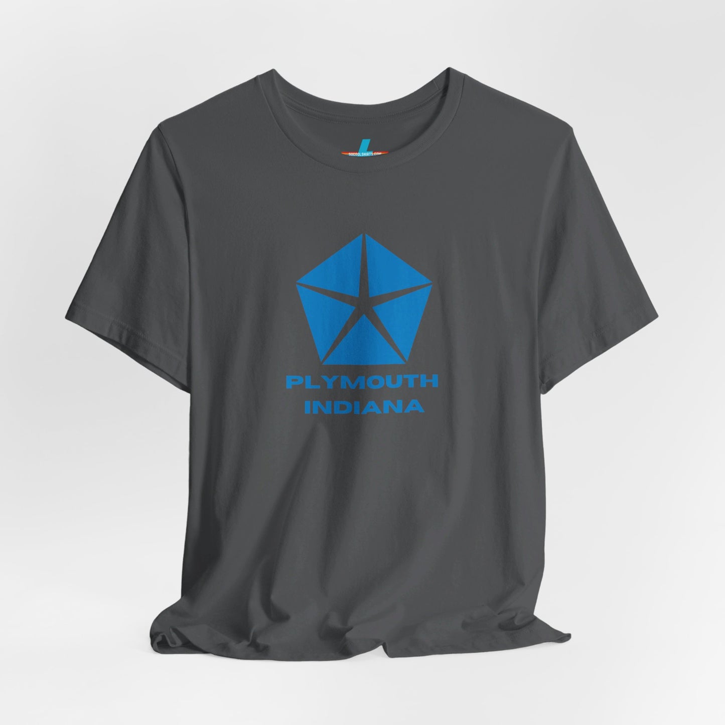 A black Printify Plymouth, Indiana Chrysler Logo T-shirt is displayed against a plain white background. The shirt features a blue, five-point star emblem reminiscent of a vintage autos design above the text "PLYMOUTH INDIANA" in blue, centered across the front. The shirt is laid out flat with the sleeves slightly bent.