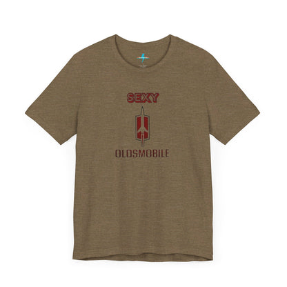 Introducing the Sexy Oldsmobile - Unisex Jersey Short Sleeve Tee by Printify, a light gray t-shirt featuring a striking graphic in the center. The design includes the word "SEXY" in bold red letters above a vertical Oldsmobile logo, underlined by the word "OLDSMOBILE" in red letters. This t-shirt is perfect for vintage car enthusiasts and comedy lovers alike, with its plain white background accentuating the bold design.