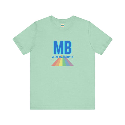 The Miller Beach Pride - Unisex Jersey Short Sleeve Tee by Printify is a white shirt made from 100% Airlume combed cotton. It showcases a design with large, bold blue letters "MB" at the top. Beneath it, the text "MILLER BEACH GARY, IN" is written in blue. A colorful, triangular rainbow graphic extends downward from the text, symbolizing Miller Beach pride.