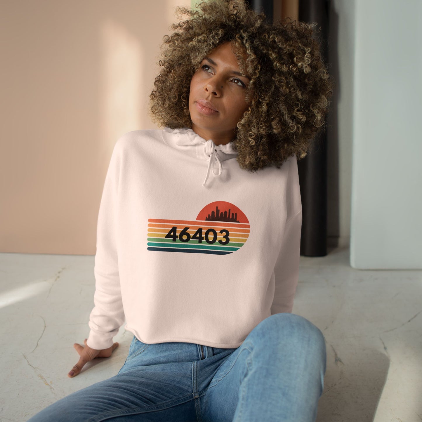 The Miller Beach 46403 Women's Crop Hoodie by Printify features a nostalgic design with a city skyline silhouette and the iconic "46403" zip code, set against a striped sunset backdrop in vibrant orange, green, and yellow hues that capture the essence of Miller Beach.