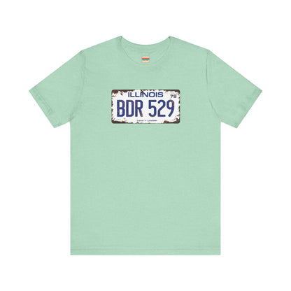 The Printify Blues Brothers BDR 529 License Plate Unisex Jersey Short Sleeve Tee showcases a vintage Illinois license plate graphic with "BDR 529" prominently displayed, as famously seen in the Blues Brothers film. The design includes "Illinois" and "Land of Lincoln" above and below the numbers, with a weathered, rustic look that enhances its retro appeal.