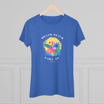 A women's triblend tee from Printify, the Miller Beach Flamingo features a blue color and "Miller Beach Gary, IN 46403" text with a vibrant design of a flamingo amidst tropical foliage for a vintage aesthetic. This t-shirt is showcased on a wooden surface alongside a denim jacket, white sneakers, and a potted plant.