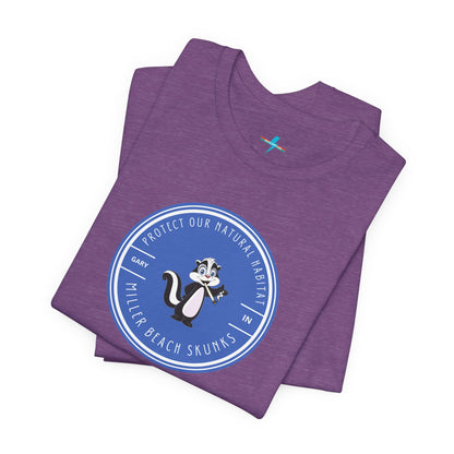 The Printify Miller Beach Skunks - Unisex Jersey Short Sleeve Tee is a gray T-shirt that features a circular blue logo at the center. Inside the logo, there is an illustration of a skunk with the text "Protect Our Habitat" and "Miller Beach Skunks" around the border, promoting environmental consciousness. The upper left part of the logo reads "Gary, IN.